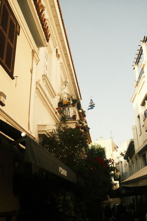 Free A picturesque alley in Greece with traditional buildings and a Greek flag against a clear sky. Stock Photo