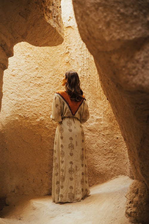 A Woman in Long Sleeve Dress Standing Beside the Brown Rock