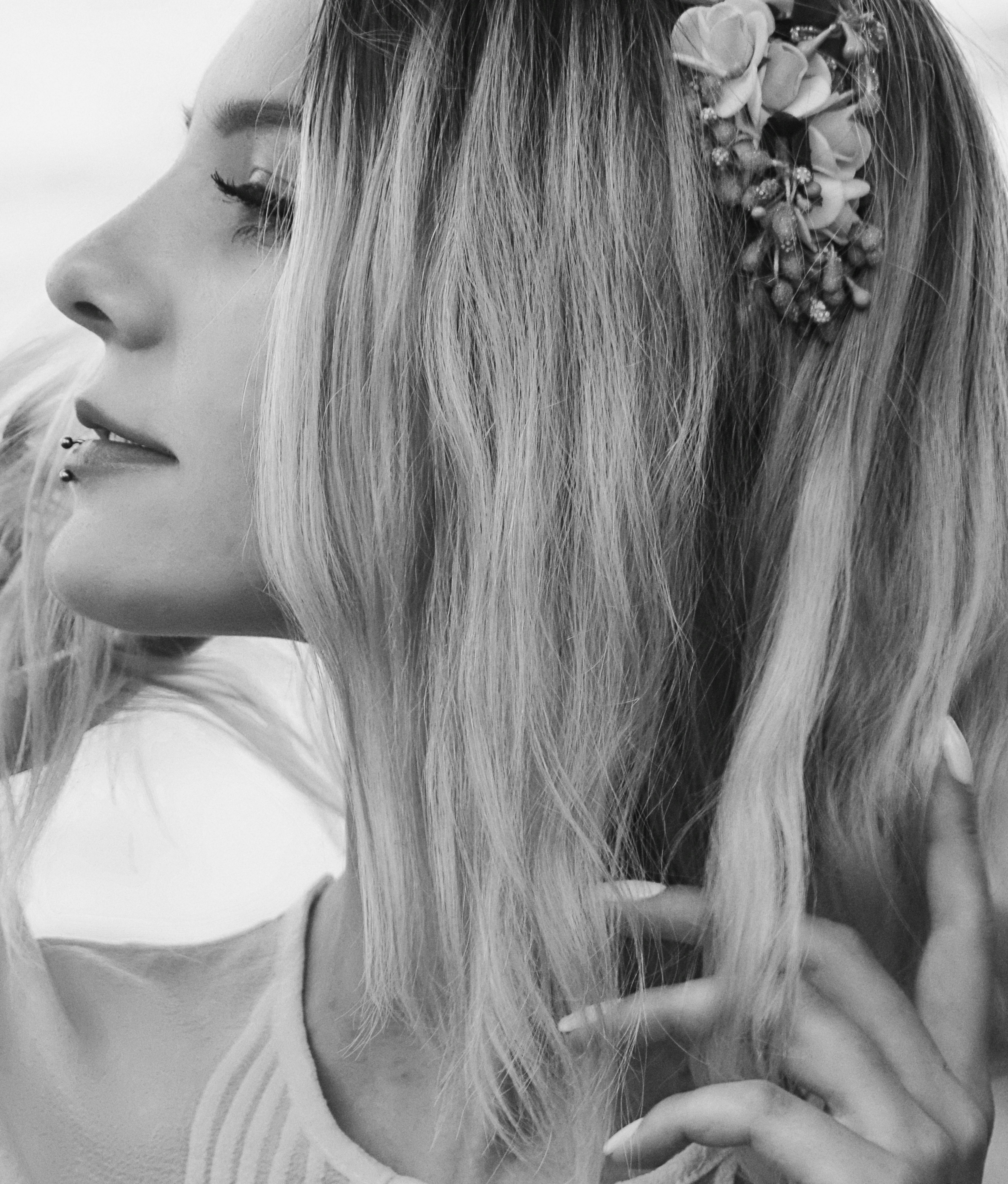 Artistic side view portrait of a woman with a floral hairpiece, emphasizing her lip piercing and serene expression.