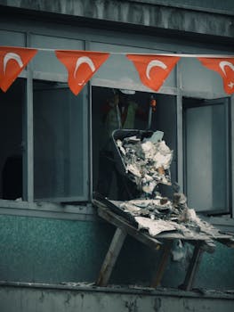 Worker throwing construction debris from a building window decorated with Turkish flags.