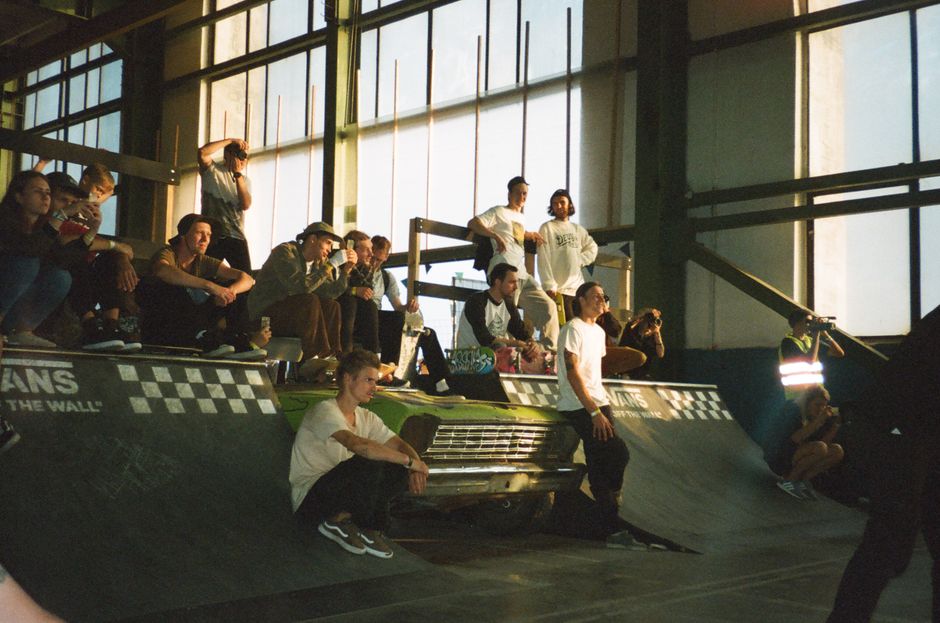 A group of people gather at an indoor skatepark, watching a skateboarding event.
