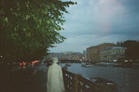 在一个宁静的河边夜晚，有建筑物、船只和一个穿着外套的孤独身影