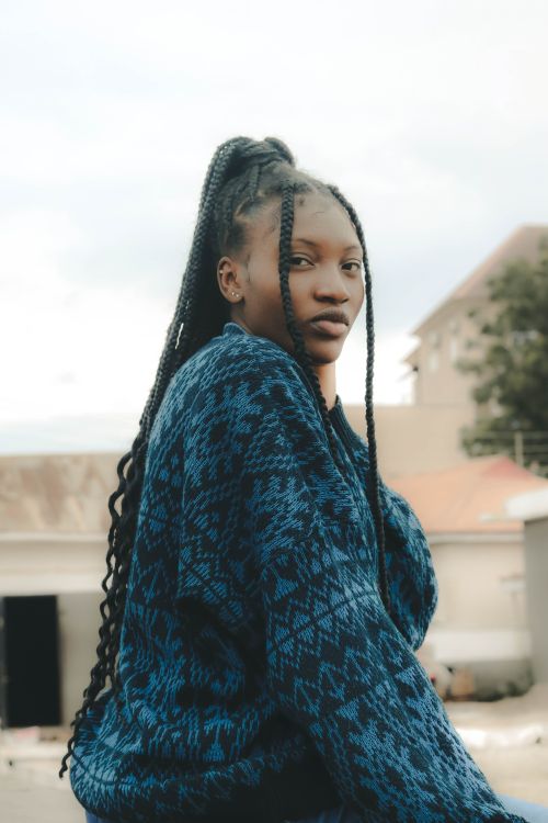 Free Portrait of a young woman with braided hair, wearing a blue sweater, sitting outside. Stock Photo