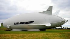 A large Airlander hybrid airship parked on a grassy field under a cloudy sky.