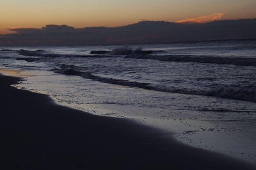 Free A serene view of a beach at twilight with gentle waves lapping the shore. Stock Photo