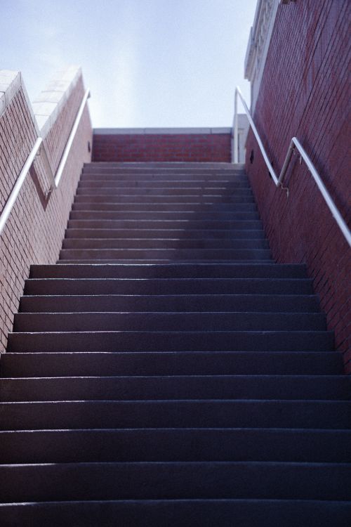 Free A low-angle view of a brick staircase with metal railings, leading outdoors under a clear sky. Stock Photo