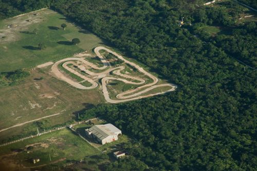Free Drone shot of a winding race track surrounded by lush green landscape, featuring a barn and cropland. Stock Photo