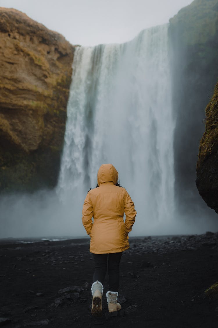 Back Of A Woman Walking Towards A Waterfall