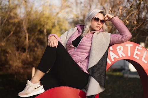 A Woman in Pink Puffer Jacket Sitting while Wearing Sunglasses