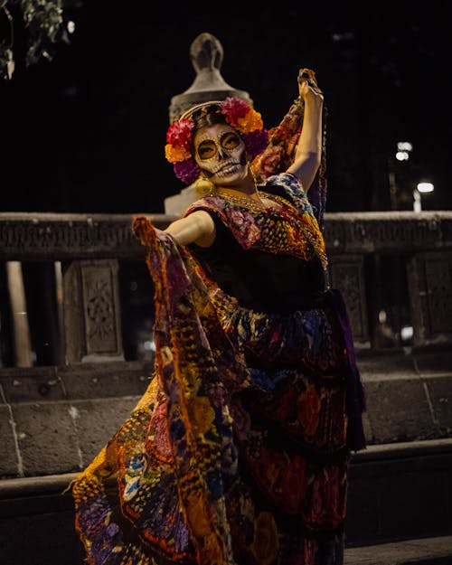 A Woman in Printed Dress with Painting on Her Face Standing on the Street at Night