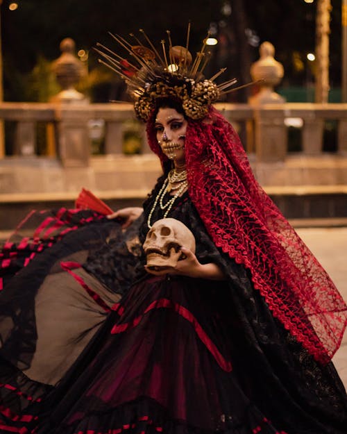 A Woman in Red and Black Dress Holding a Skull while Standing on the Street