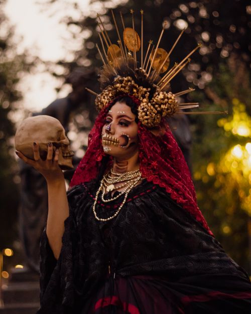 Free A woman in traditional Day of the Dead attire holds a skull with intricate face paint and a vibrant headdress. Stock Photo