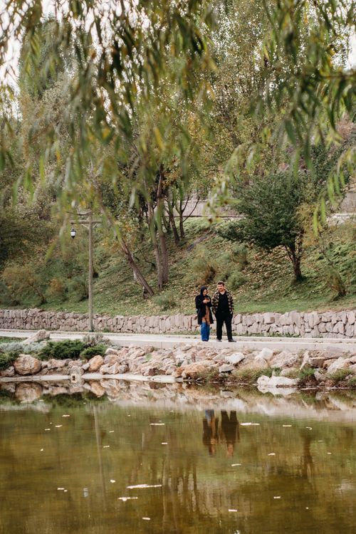 Free A couple strolling by a serene pond in a lush, green park setting. Stock Photo