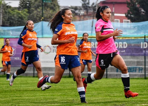 Action shot of women athletes playing soccer outdoors on a sunny day.