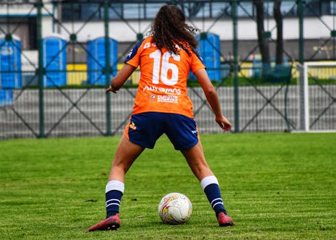 Female soccer player wearing orange and blue sportswear on a grassy field preparing to make a play.