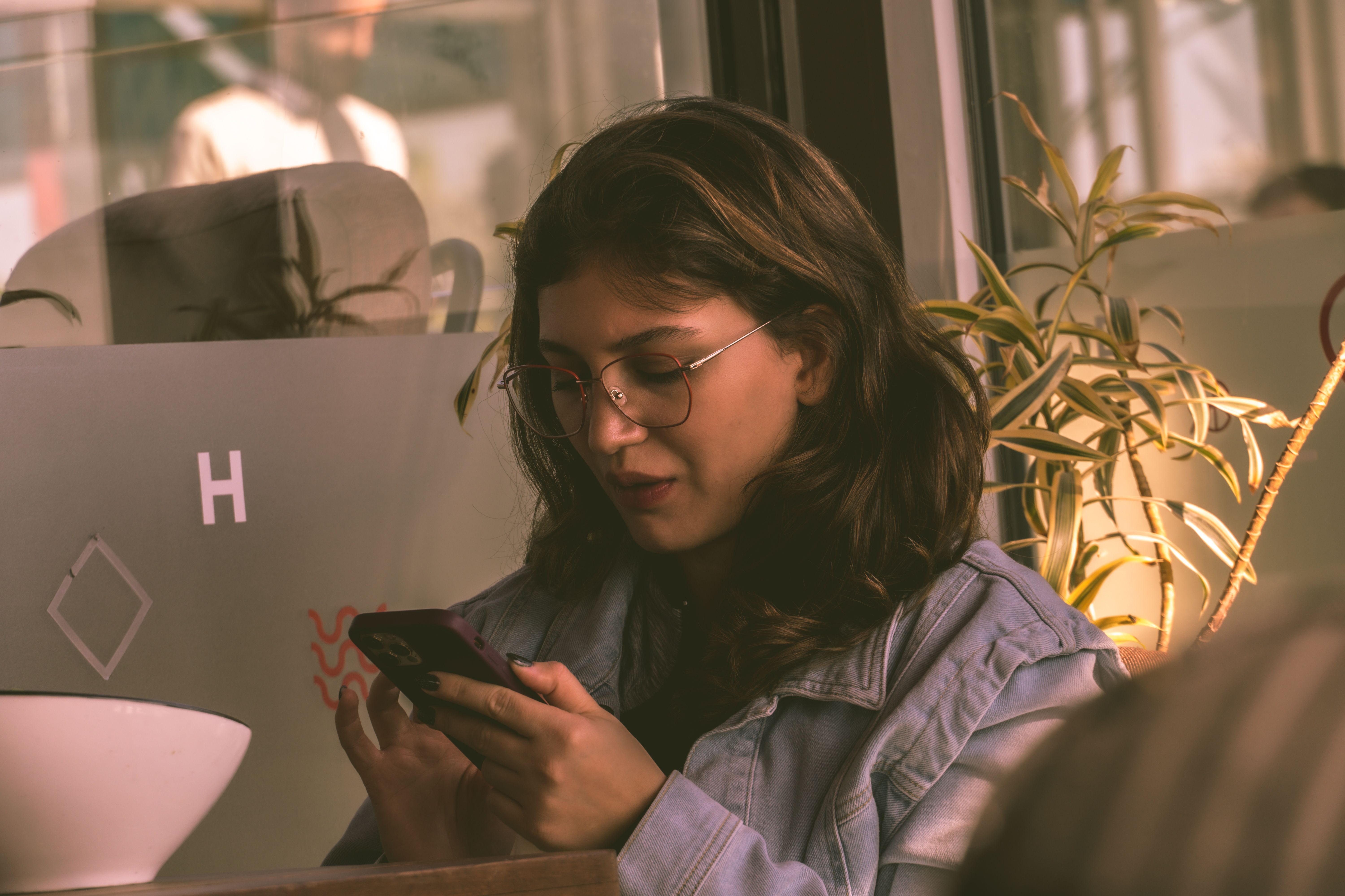 A young person holding a smartphone with a Bible app open, sitting in a coffee shop, looking contemplative