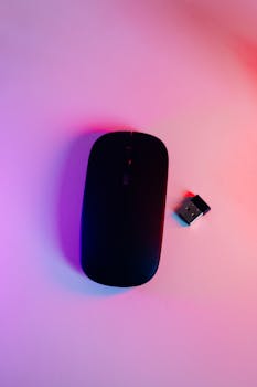 A sleek black wireless mouse with a USB adapter on a colorfully lit surface.