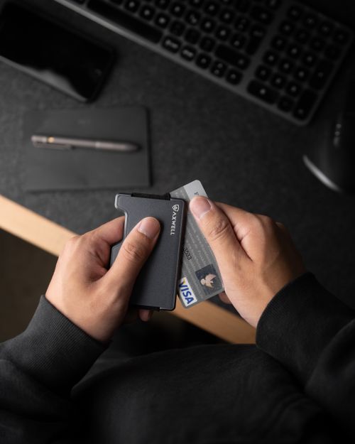 Free A close-up of hands holding a sleek minimalist metal wallet containing ID and credit card. Stock Photo