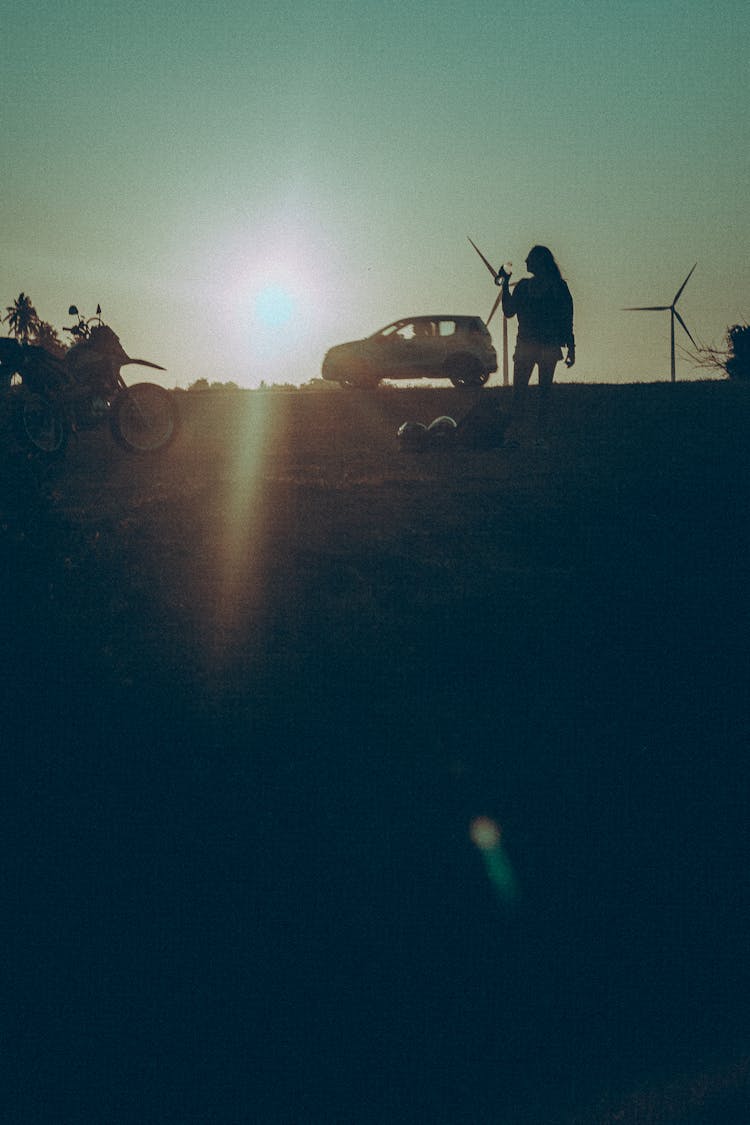 Silhouettes Of A Person, A Car And A Motorcycle At Sunset