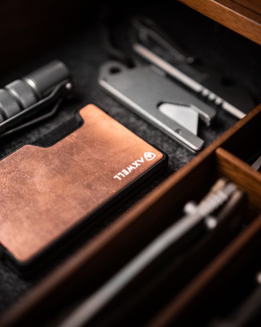 A wallet and everyday carry essentials neatly arranged in a wooden drawer