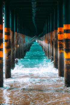 Capture the dynamic waves and rustic charm of a wooden pier at sea, with a dramatic perspective.