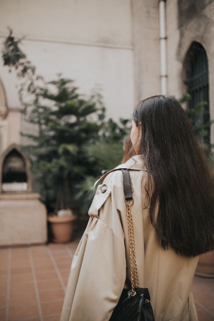 Young woman in fashionable trench coat exploring an outdoor courtyard.