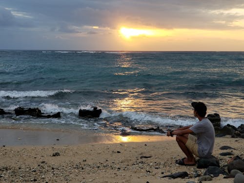 Mann, Der Am Strand Sitzt Und Untergehende Sonne Betrachtet