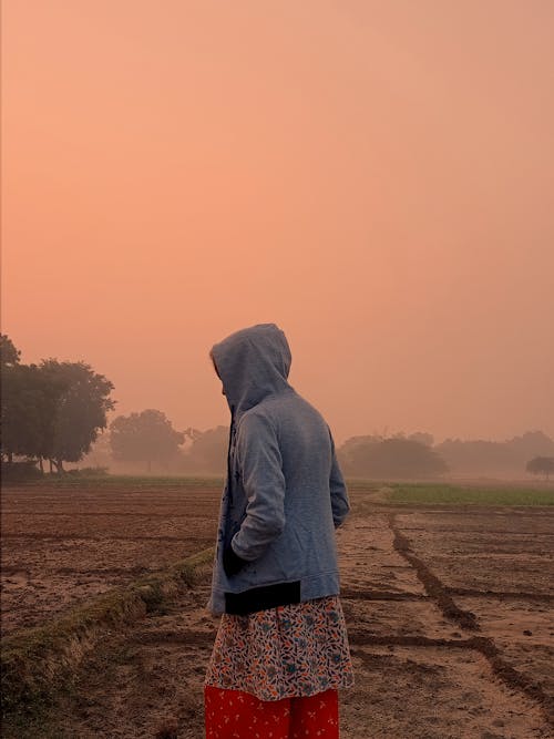 Woman in Hoodie Walking in Field on Sunset