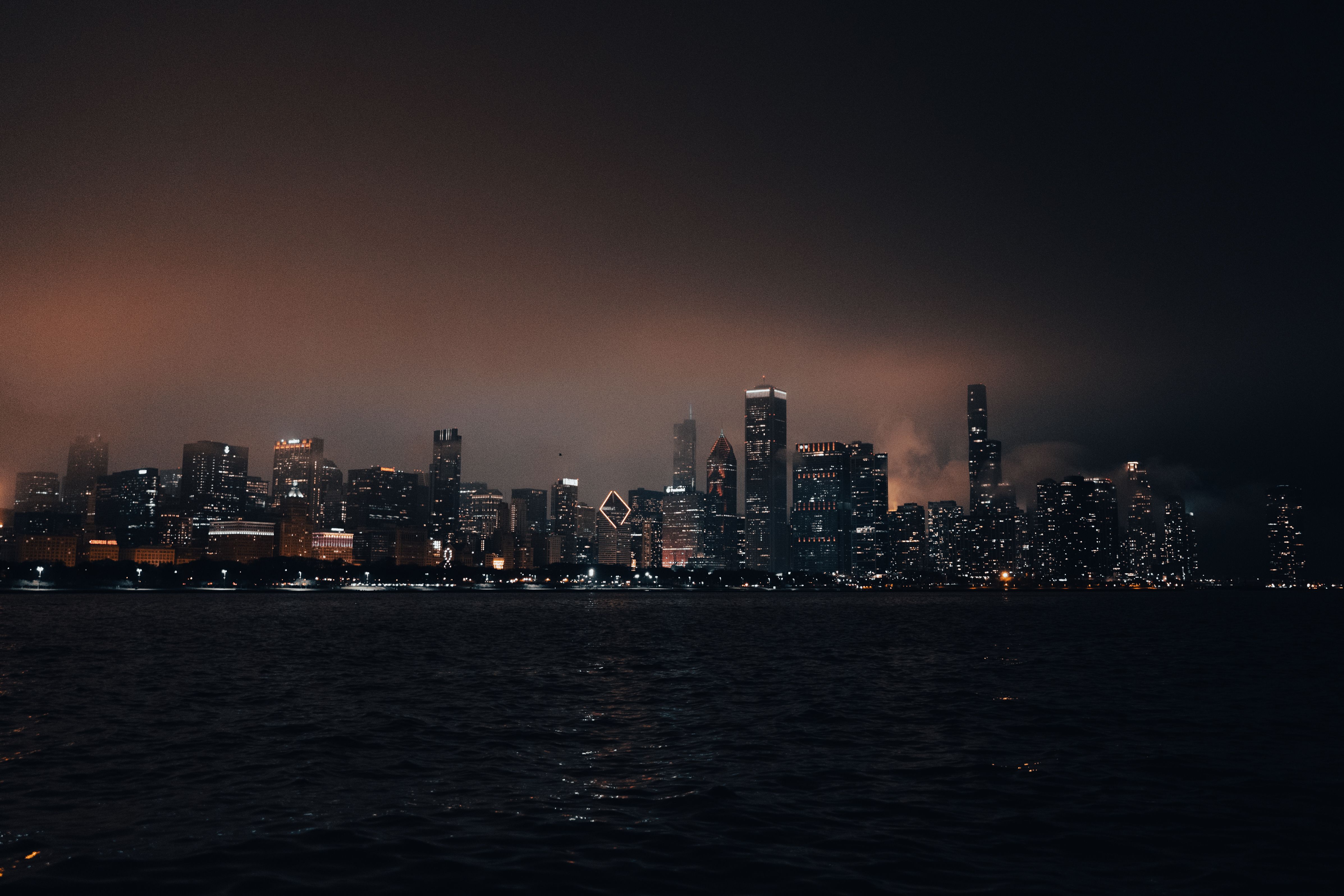 A moody and dramatic view of Chicago's skyline at night with city lights reflecting on the water.