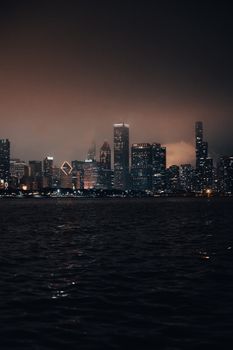 Beautiful illuminated city skyline at night with reflections on water, showcasing a vibrant urban atmosphere.