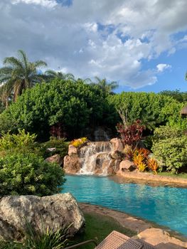 Lush tropical garden with a serene waterfall flowing into a turquoise pool, ideal for relaxation.
