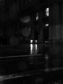 Black and white photo of a car on a rainy night in New York City.