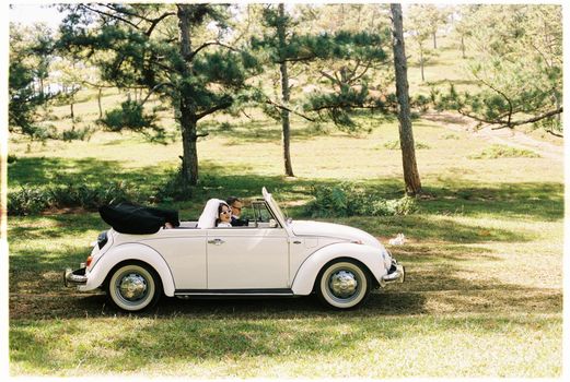 A couple in a classic white convertible enjoying a sunny day in a park.