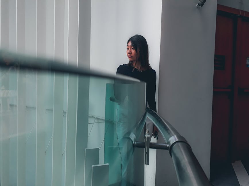 A woman in a modern indoor space, standing by glass railings, conveying a thoughtful mood.