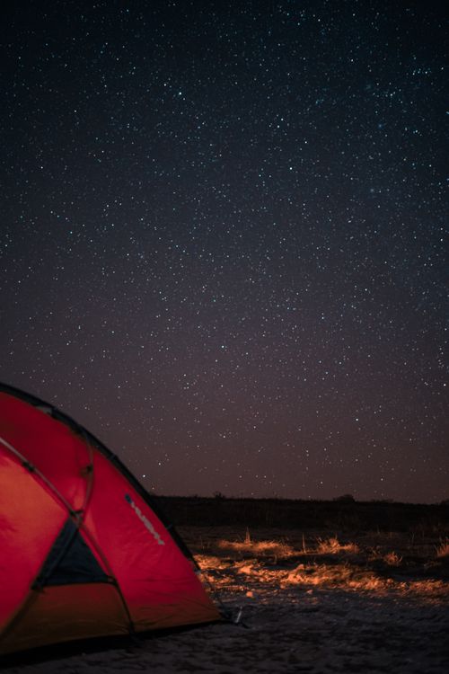 Free A serene night camping under a star-filled sky with a glowing red tent. Stock Photo