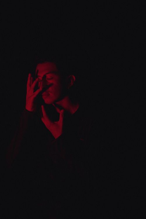 Free A dramatic portrait with red light focusing on expression and mood through hands and shadows. Stock Photo