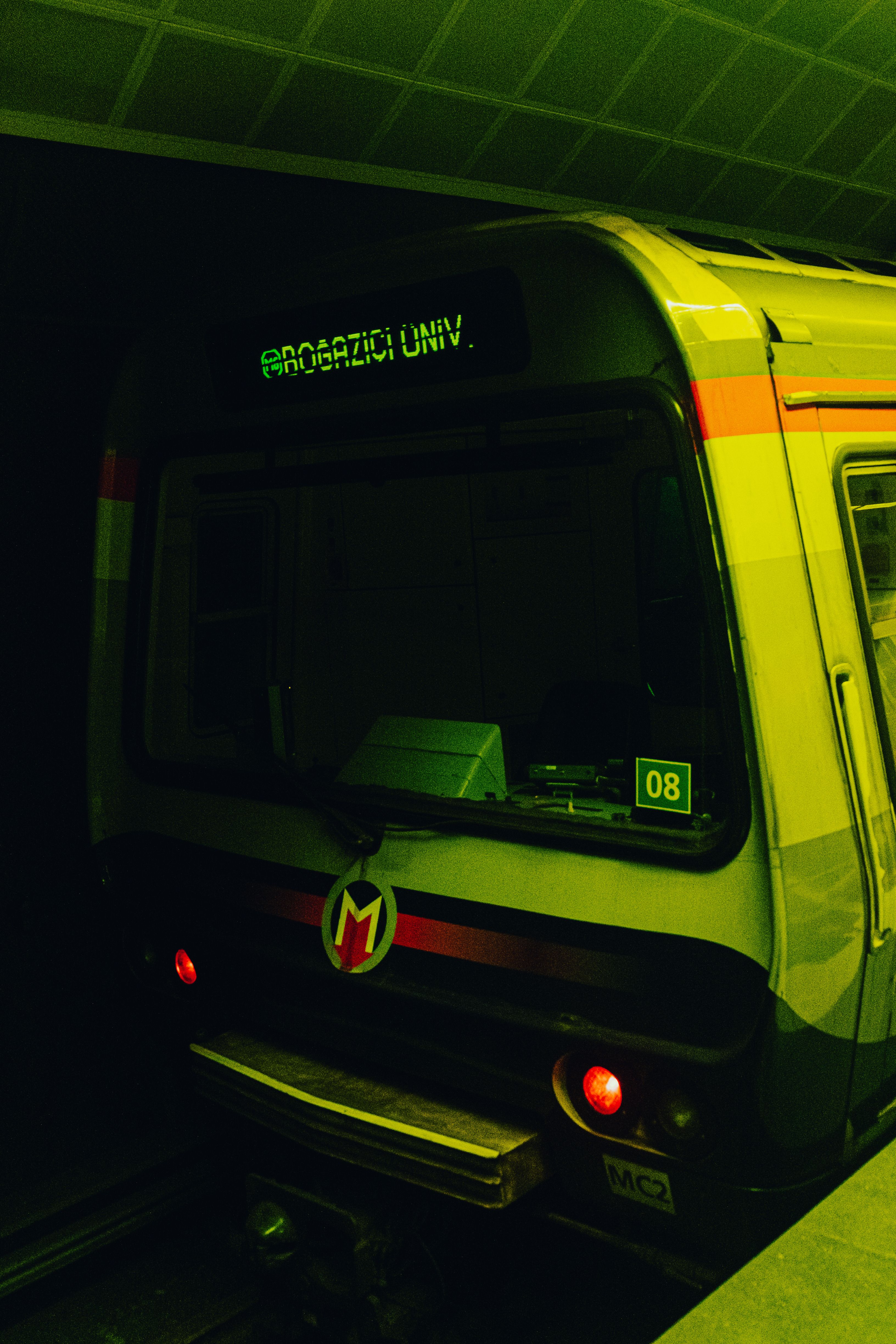 Night view of a modern subway train with Boğaziçi Univ displayed, awaits departure from the metro station.