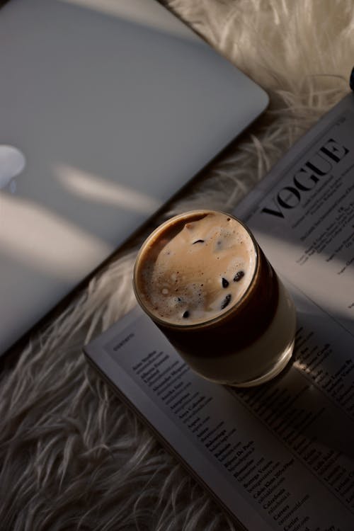 A Glass of Iced Cappuccino on a Magazine Beside a Laptop`