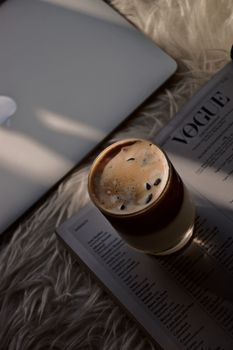 Stylish iced coffee on a magazine with a laptop, perfect for relaxing or work-from-home vibes.