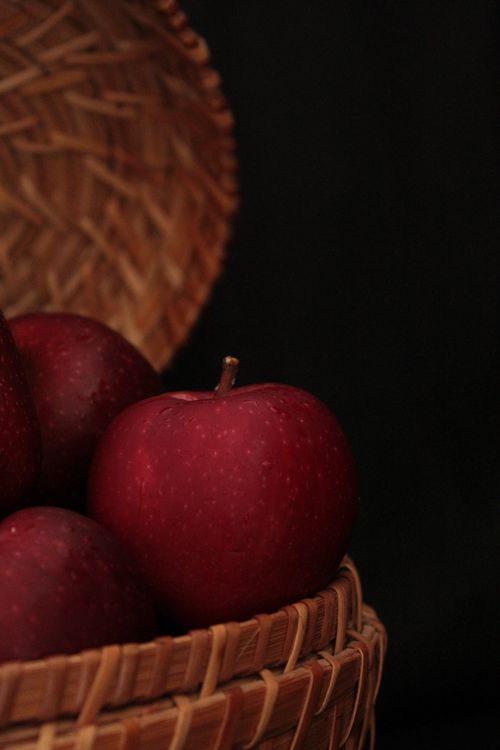 Free A close-up view of fresh red apples placed in a woven basket against a dark background. Stock Photo