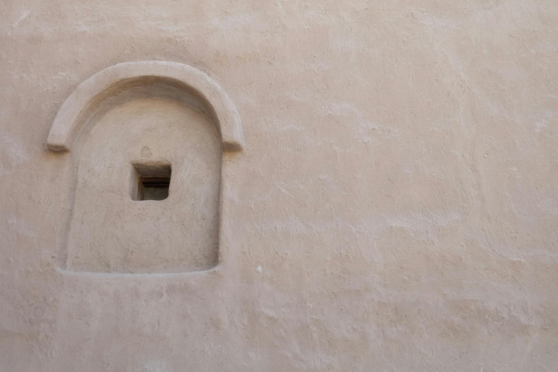 A close-up of a minimalist arched window in a traditional sand-colored Dubai structure.