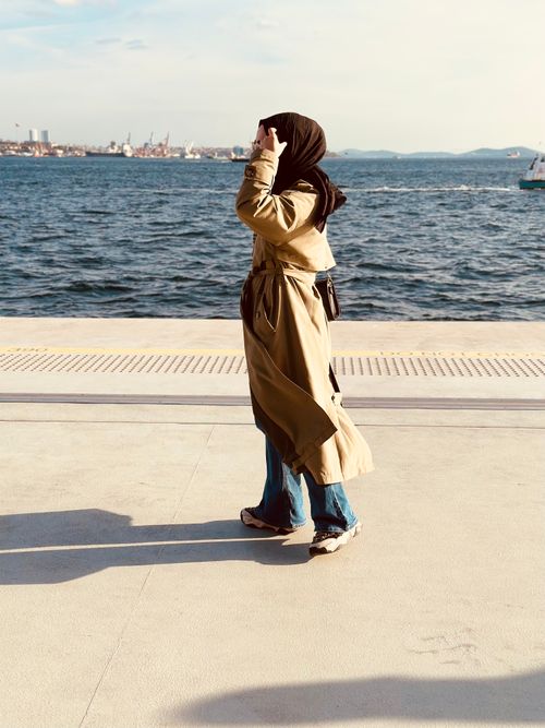 Free A woman in a hijab and trench coat walking by the sea in İstanbul. Stock Photo