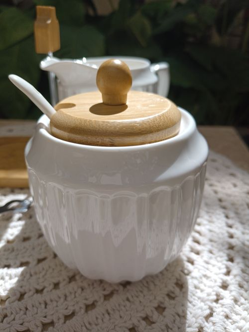Free White ceramic condiment jar with wooden lid on a crochet mat, bathed in natural light. Stock Photo