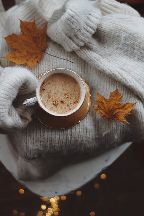 Coffee Cup and Autumn Leaves on a Sweater · Free Stock Photo