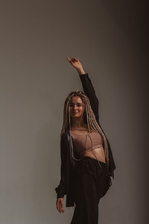 Woman with Dreadlocks Posing against Gray Background with a Raised Hand