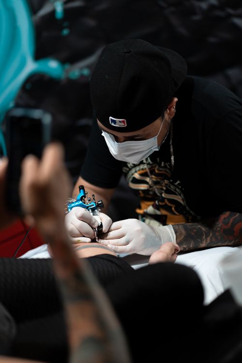 Free Tattoo artist with face mask and gloves tattooing a client in a professional studio. Stock Photo