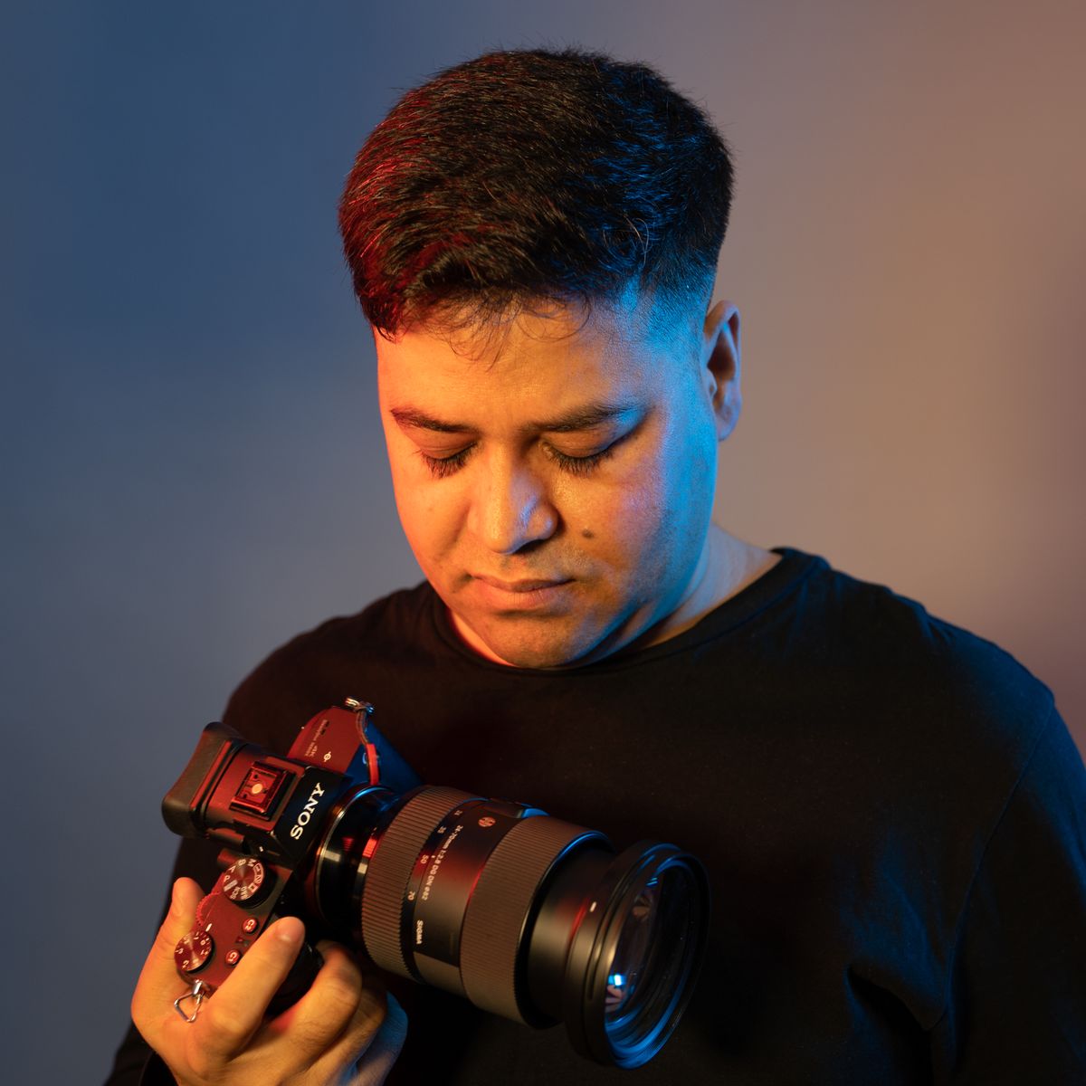 Profesjonalny fotograf trzyma aparat DSLR w studyjnym oświetleniu, patrzący w obiektyw — dramatyczne barwne światło w tle