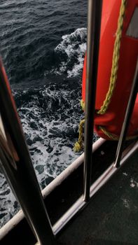 View of ocean waves alongside a life ring by a metal fence on a ship.
