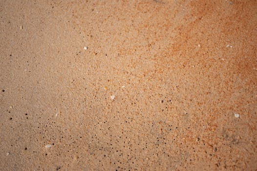Detailed macro shot of a sandy beach surface in Albufeira, Portugal, showcasing intricate textures and hues.