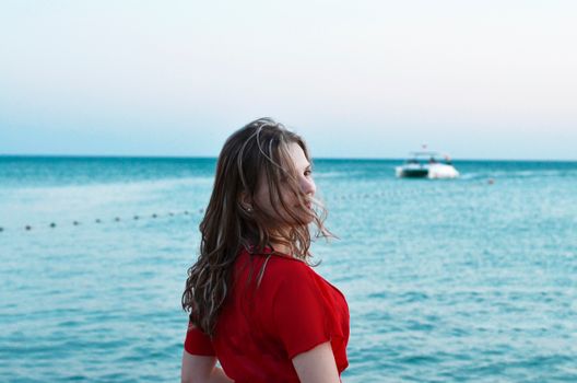 一位身穿红色连衣裙的女子在游艇旁静静欣赏海滩日落
